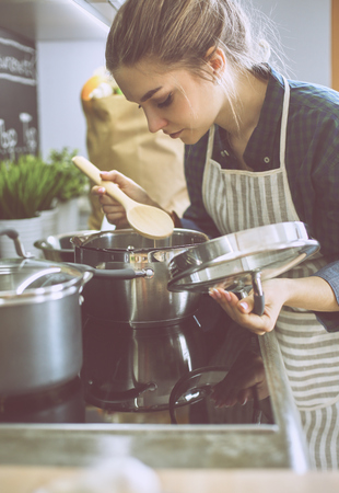 Young woman cooking in her kitchen standing near stoveの写真素材