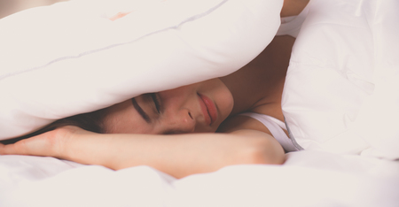 Female lying on bed and closing her ears with pillowの写真素材