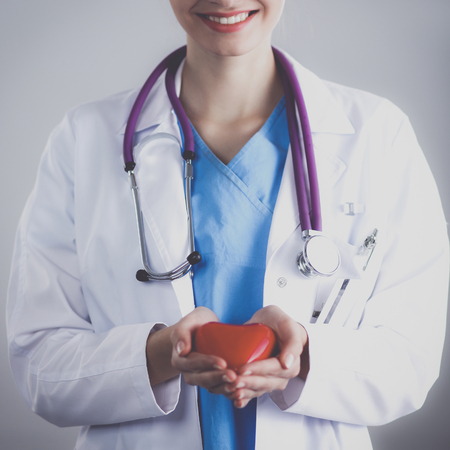 Young woman doctor holding a red heart, standing in hospitalの写真素材