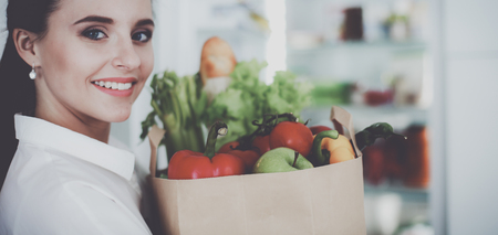 Young woman holding grocery shopping bag with vegetables .Standing in the kitchenの写真素材