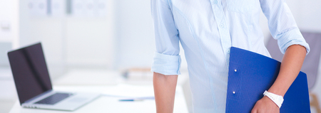Attractive young businesswoman standing near desk with folder in the officeの写真素材