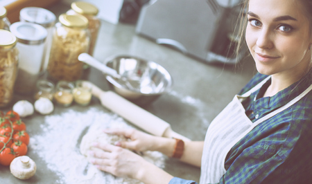 Beautiful woman cooking cake in kitchen standing near deskの写真素材