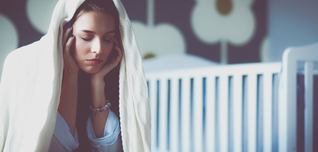 Young tired woman sitting on the bed near childrens cotの写真素材