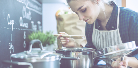 Young woman cooking in her kitchen standing near stoveの写真素材