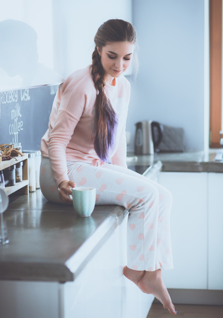 Young woman sitting on table in the kitchenの写真素材