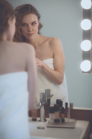 Young woman looking in the mirror and putting make-up onの写真素材