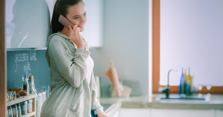 Woman using mobile phone sitting in modern kitchenの写真素材