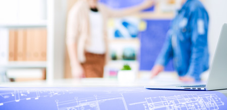 Two young woman standing near desk with instruments, plan and laptopの写真素材