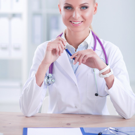 Beautiful young smiling female doctor sitting at the desk and writing.の写真素材