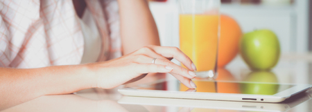 Woman using a tablet computer while drinking juice in her kitchenの写真素材