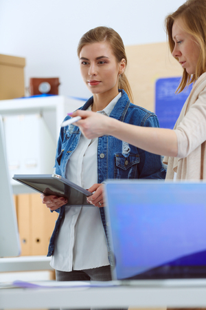 Two young woman standing near desk with instruments, plan and laptop.の写真素材