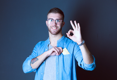 Young man holding a credit card standing on gray background. Youの写真素材