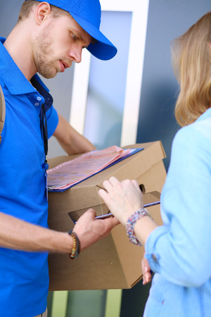 Smiling delivery man in blue uniform delivering parcel box to recipient - courier service conceptの写真素材