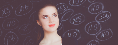 Young woman is standing on blackboard background and thinking: yes or noの写真素材