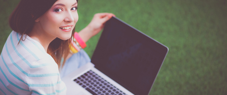 Young woman with laptop sitting on green grassの写真素材