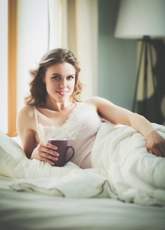 Young woman drinking cup of coffee or tea while lying in bed.の写真素材
