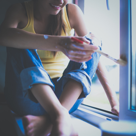 Woman painting wall of an apartment with a paintbrush carefully finishing off around  window frameの写真素材