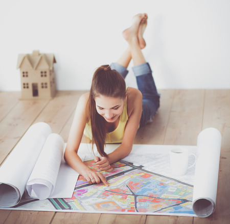 Young woman lying on the floor and looking at blueprint of new houseの写真素材