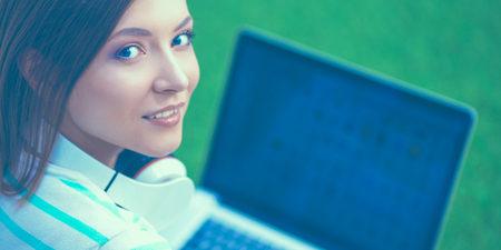 Young woman with laptop sitting on green grassの写真素材