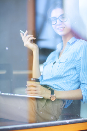Young woman sitting at office table with laptop,view through window. Young womanの写真素材