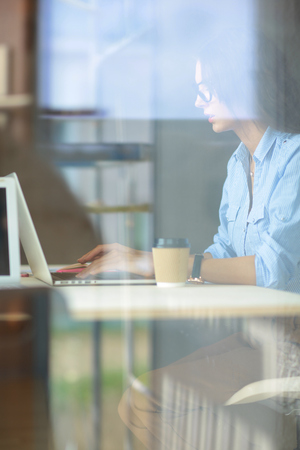 Young woman sitting at office table with laptop,view through window. Young womanの写真素材