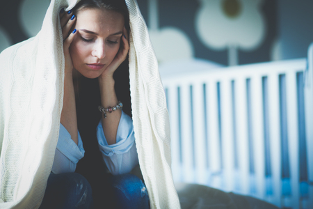 Young tired woman sitting on the bed near childrens cot. Young mom.の写真素材