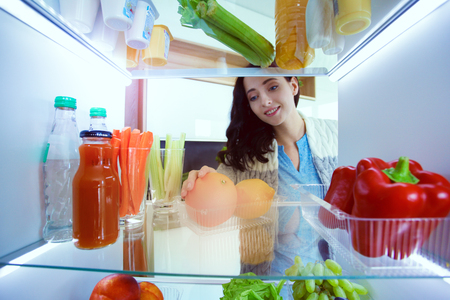 Portrait of female standing near open fridge full of healthy food, vegetables and fruits. Portrait of femaleの写真素材