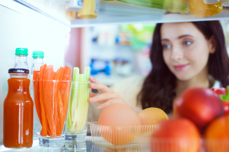 Portrait of female standing near open fridge full of healthy food, vegetables and fruits. Portrait of femaleの写真素材