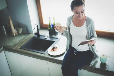 Beautiful young woman using a digital tablet in the kitchen.の写真素材