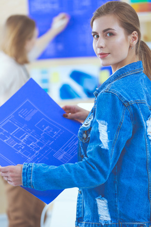 Two young woman standing near desk with instruments, plan and laptop.の写真素材