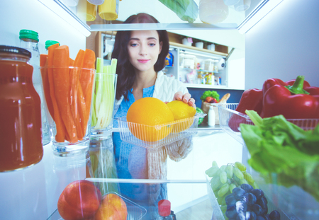 Portrait of female standing near open fridge full of healthy food, vegetables and fruits. Portrait of femaleの写真素材