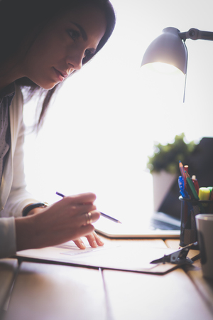 Young female working sitting at a desk. Businesswoman. Drawing. Student. Workplace. Desk.の写真素材
