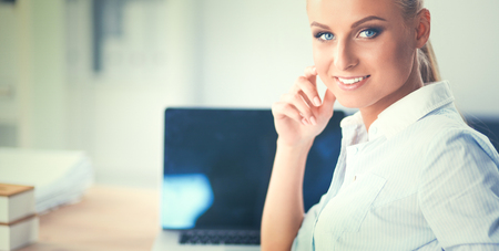 Attractive businesswoman sitting on a desk with laptop in the officeの写真素材