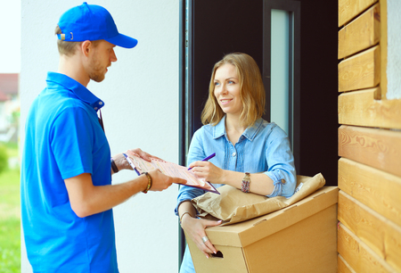 Smiling delivery man in blue uniform delivering parcel box to recipient - courier service concept. Smiling delivery man in blue uniformの写真素材