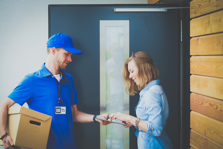 Smiling delivery man in blue uniform delivering parcel box to recipient - courier service concept. Smiling delivery man in blue uniformの写真素材