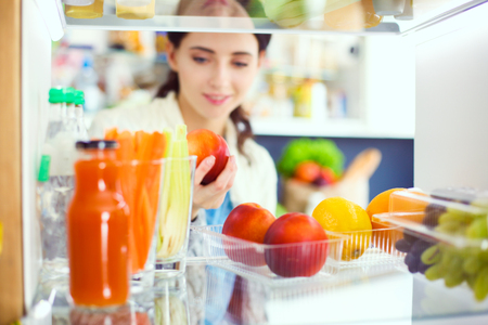 Portrait of female standing near open fridge full of healthy food, vegetables and fruits. Portrait of femaleの写真素材