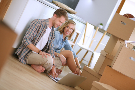 Young couple moving in new home.Sitting and relaxing after unpacking.Looking something on laptop. Young coupleの写真素材