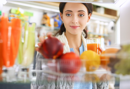 Portrait of female standing near open fridge full of healthy food, vegetables and fruits. Portrait of femaleの写真素材