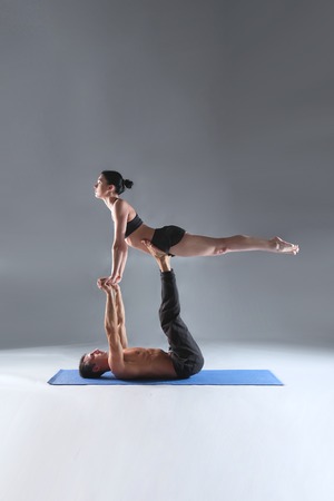 Young couple practicing acro yoga on mat in studio together. Acroyoga. Couple yoga. Partner yoga.の写真素材
