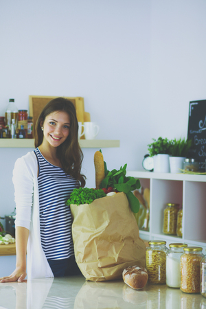Young woman holding grocery shopping bag with vegetables .Standing in the kitchen. Young womanの写真素材