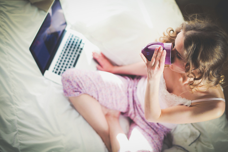 Young beautiful woman sitting in bed with laptop.の写真素材