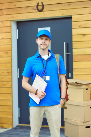 Smiling delivery man in blue uniform delivering parcel box to recipient - courier service concept. Smiling delivery man in blue uniformの写真素材