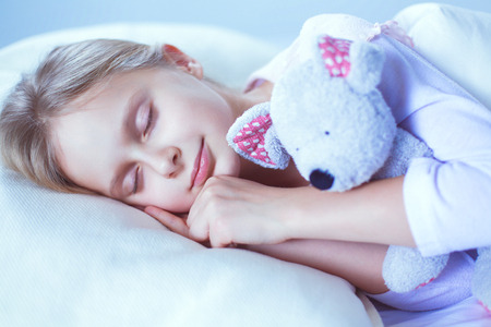 Child little girl sleeps in the bed with a toy teddy bearの写真素材