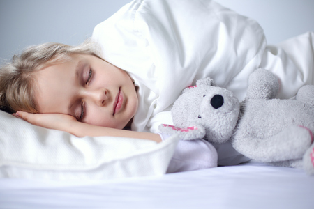Child little girl sleeps in the bed with a toy teddy bearの写真素材
