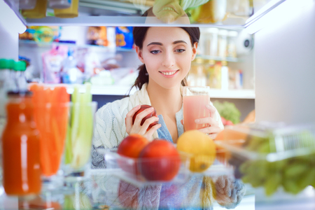 Portrait of female standing near open fridge full of healthy food, vegetables and fruits. Portrait of femaleの写真素材