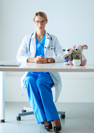 Beautiful young smiling female doctor sitting at the desk.の写真素材