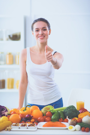 Young and cute woman sitting at the table full of fruits and vegetables in the wooden interiorの写真素材