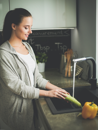 Beautiful young woman washing vegetables for salad while standing in the kitchen.の写真素材