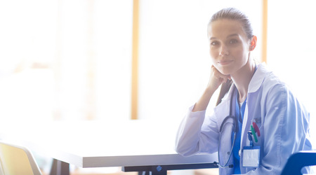 Beautiful young smiling female doctor sitting at the desk. Woman doctorの写真素材