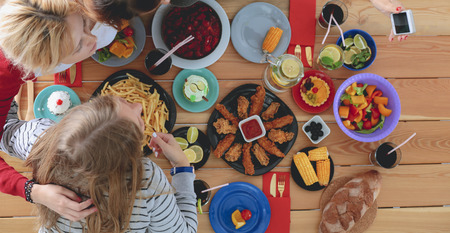 Top view of group of people having dinner together while sitting at wooden table. Food on the table. People eat fast food.の写真素材